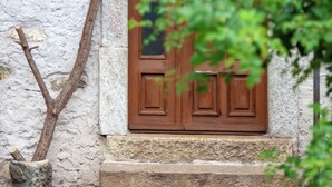 A stone building with a wooden door marked "1920" above it, a small window with a lantern, and a tree branch partially obscuring the view.
