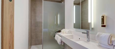 Een moderne badkamer met een douchecabine van glas, een witte wastafel met een grote spiegel en keurig opgevouwen handdoeken.