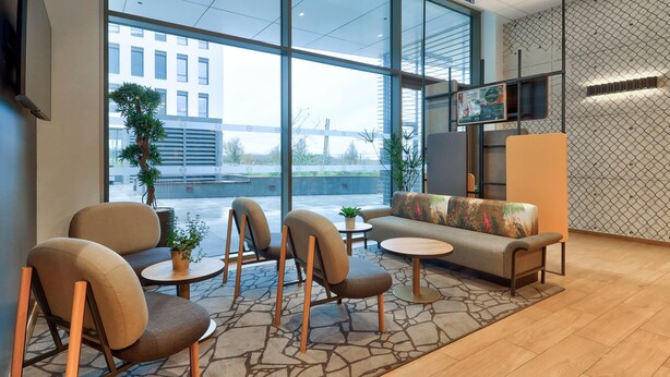 A modern hotel lobby with large windows, seating area, and a television. - B&B HOTEL Dijon Valmy Toison d'Or (Dijon)