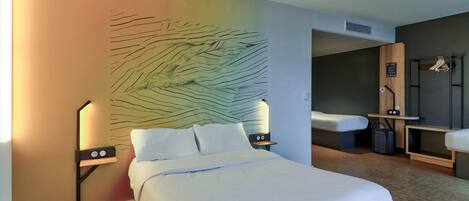 A hotel room with a bed, bedside tables, a wall art piece, a seating area, and a wardrobe.