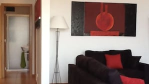 Un salon moderne avec un canapé foncé, des coussins rouges, une lampe sur pied et un tableau accroché au mur.