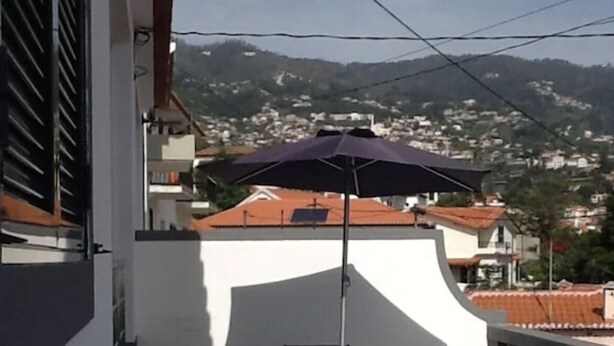 Un balcon avec une table et des chaises, un banc en bois et un parasol.
