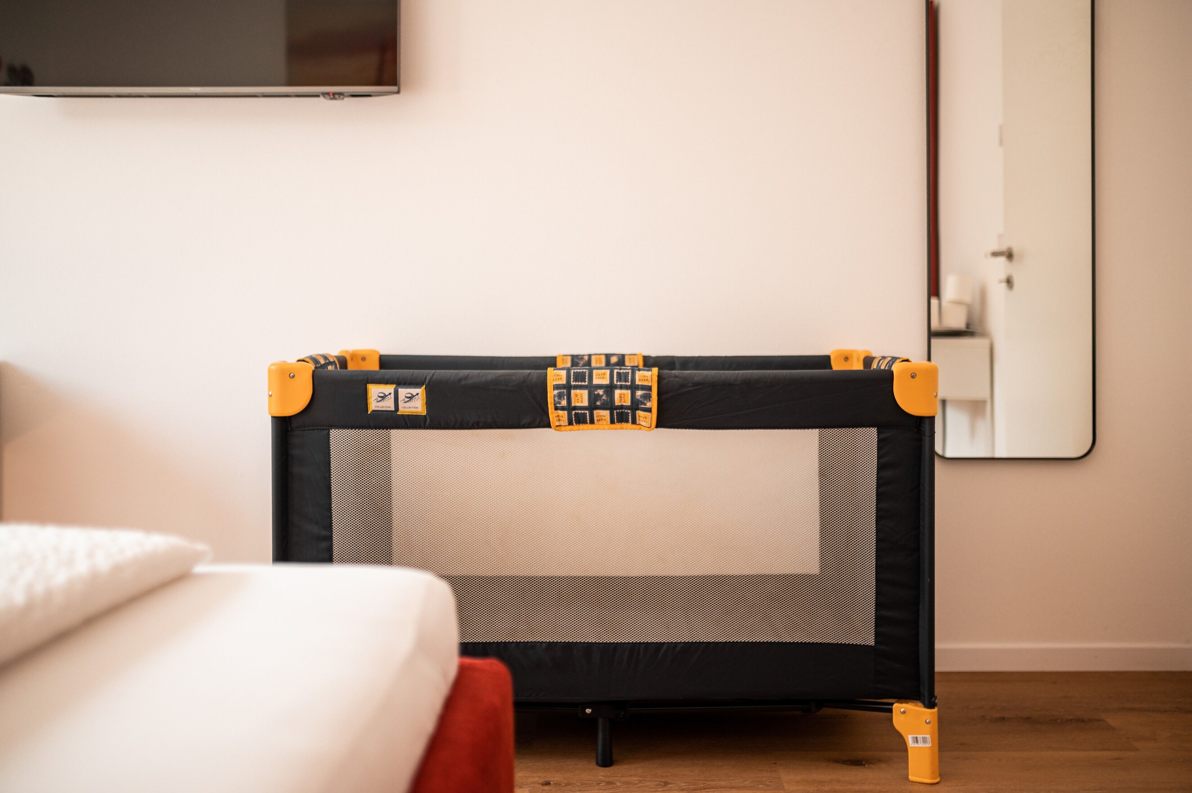 A room with a bed, a small black and yellow playpen, and a white door.
