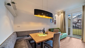 Comedor con mesa de madera, asientos acolchados, una lámpara colgante y vistas a una montaña nevada a través de una puerta de cristal.