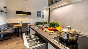 Una cocina moderna con estufa integrada, un comedor con banco y una pequeña isla con una olla.