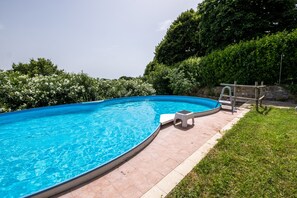 Une piscine à bord incurvé, un petit tabouret blanc et une échelle en bois.