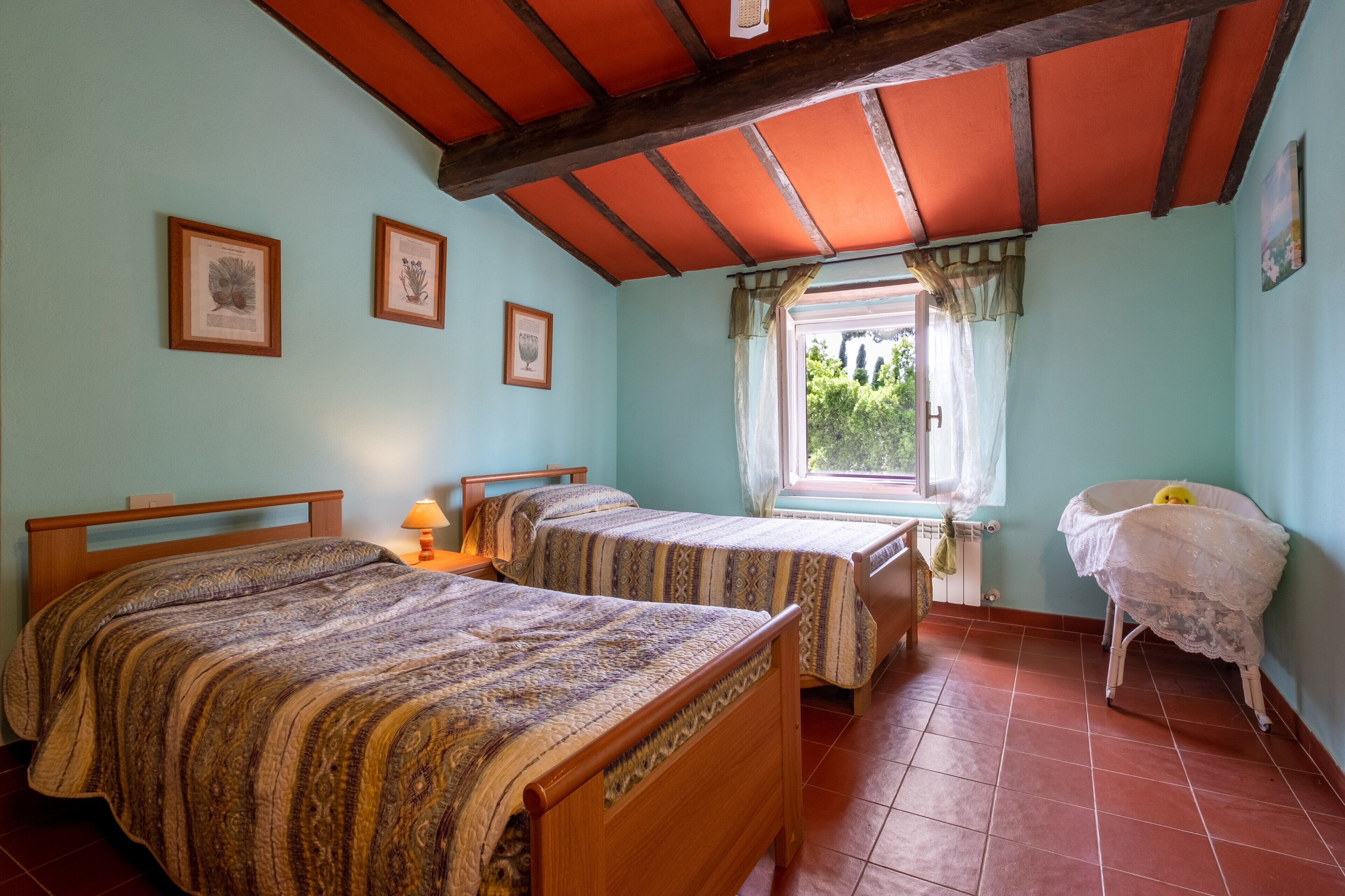 A room with two wooden beds, a window with a view, and a crib.