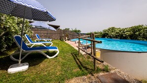 A backyard with a swimming pool, two lounge chairs, and a blue and white striped umbrella.