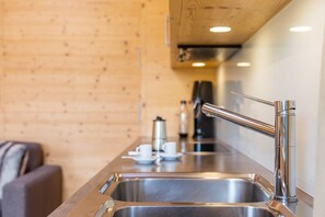 Una cocina moderna con electrodomésticos de acero inoxidable, una pared de madera y un sofá al fondo.