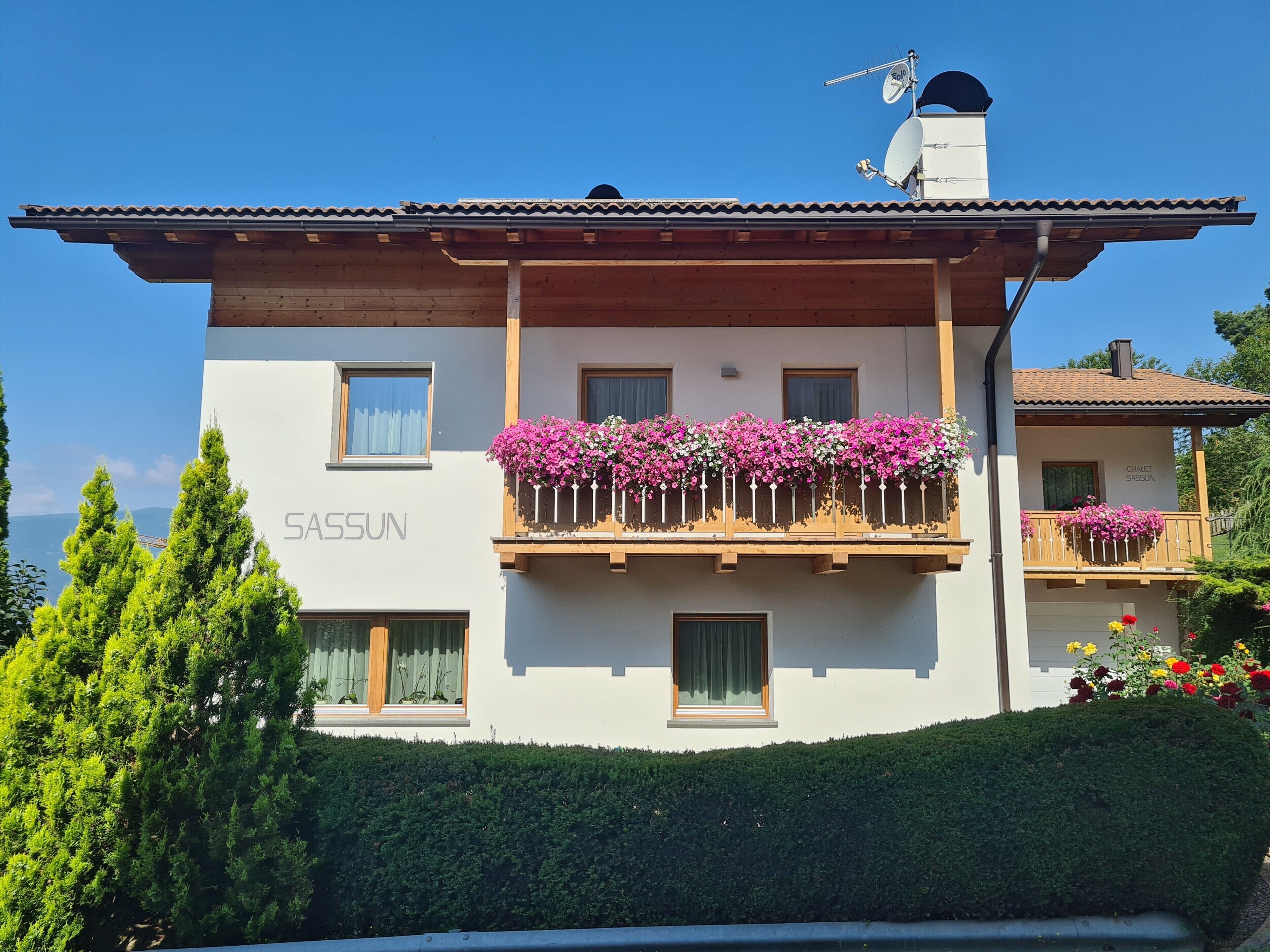 Ein zweistöckiges Gebäude mit Balkonen und einem Schild mit der Aufschrift 'SAASSUN' unter blauem Himmel.