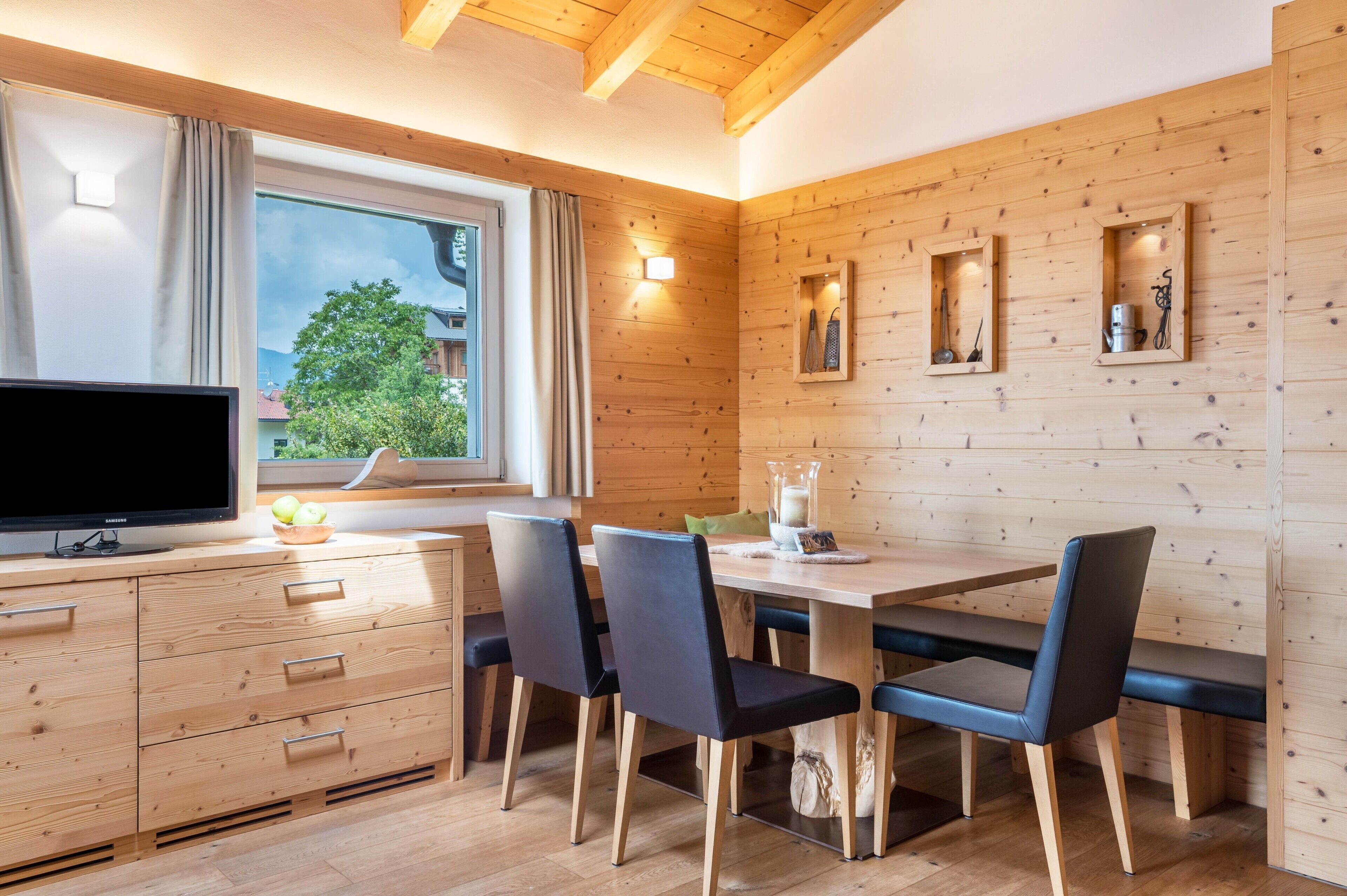 Una cucina moderna con mobili in legno, un tavolo da pranzo con sedie, una televisione e una finestra con tende.
