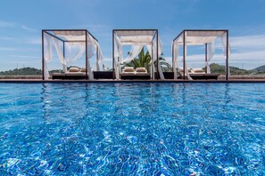 A pool with clear blue water, surrounded by three white canopy beds with white bedding.