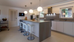 A modern kitchen with a central island, bar stools, pendant lighting, a built-in oven, and a large window.
