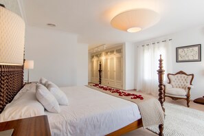 Ein Schlafzimmer mit einem großen Bett, einem Holz-Kopfende, einem Sessel, einem Kleiderschrank und einer Deckenleuchte.
