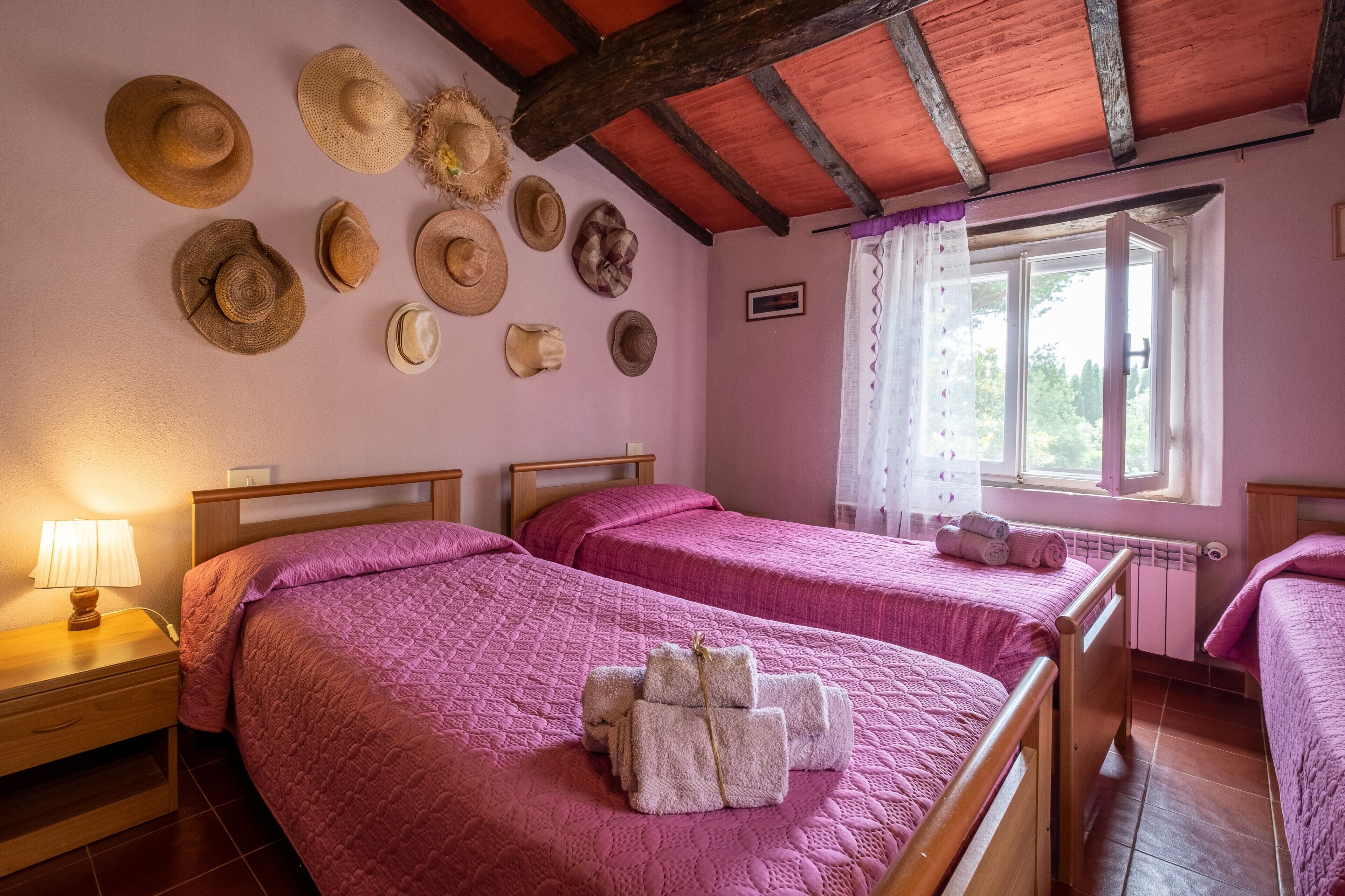 Una habitación con dos camas, una ventana con cortinas y una colección de sombreros en la pared.
