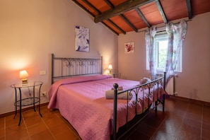 A bedroom with a bed, two bedside tables, a window with curtains, and a ceiling with exposed beams. - Apartment "Agriturismo La Pieve - Tulipani" with Shared Pool & Wi-Fi (Magliano in Toscana)