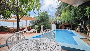Un espace aménagé au bord de la piscine, avec une table et des chaises, entouré de verdure et de parasols.
