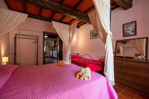 A bedroom with a bed, a wooden dresser, a mirror, and a door leading to another room.