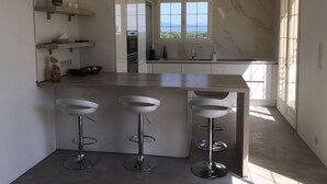 A modern kitchen with a marble backsplash, a large window, and three bar stools. - Luxury villa -private heated pool-mountain view 5 min from the sea-4 bdrms -2SDB (Serra-di-Fiumorbo (20243))