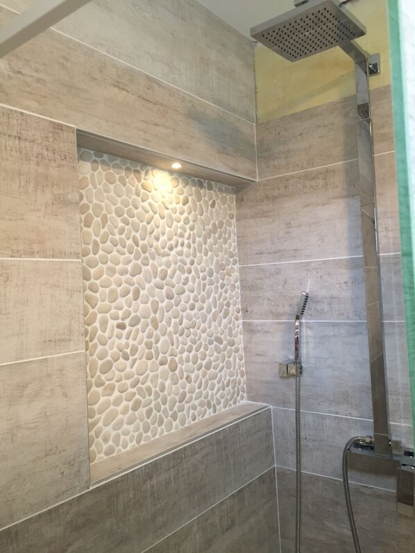 A shower area with a stone wall design and a handheld showerhead.