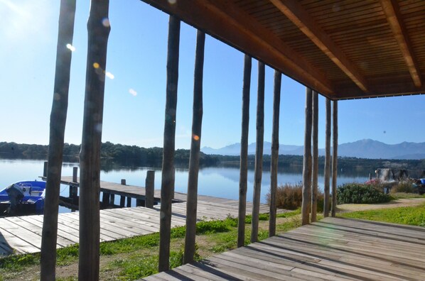 Una terraza de madera con vista a un lago tranquilo y montañas lejanas.