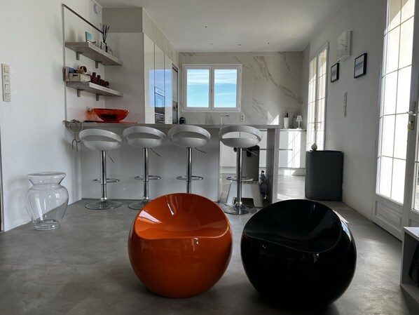 A modern kitchen with white cabinets, a large window, and a bar area with stools.