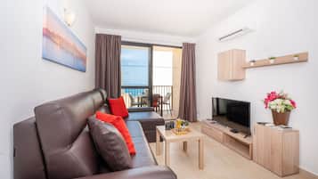 A modern living room with a leather sofa, a flat-screen TV, a coffee table, and a balcony with curtains.