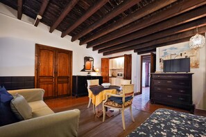 Een kamer met een houten plafond, een bank, een eettafel met stoelen, een dressoir en een schilderij aan de muur.