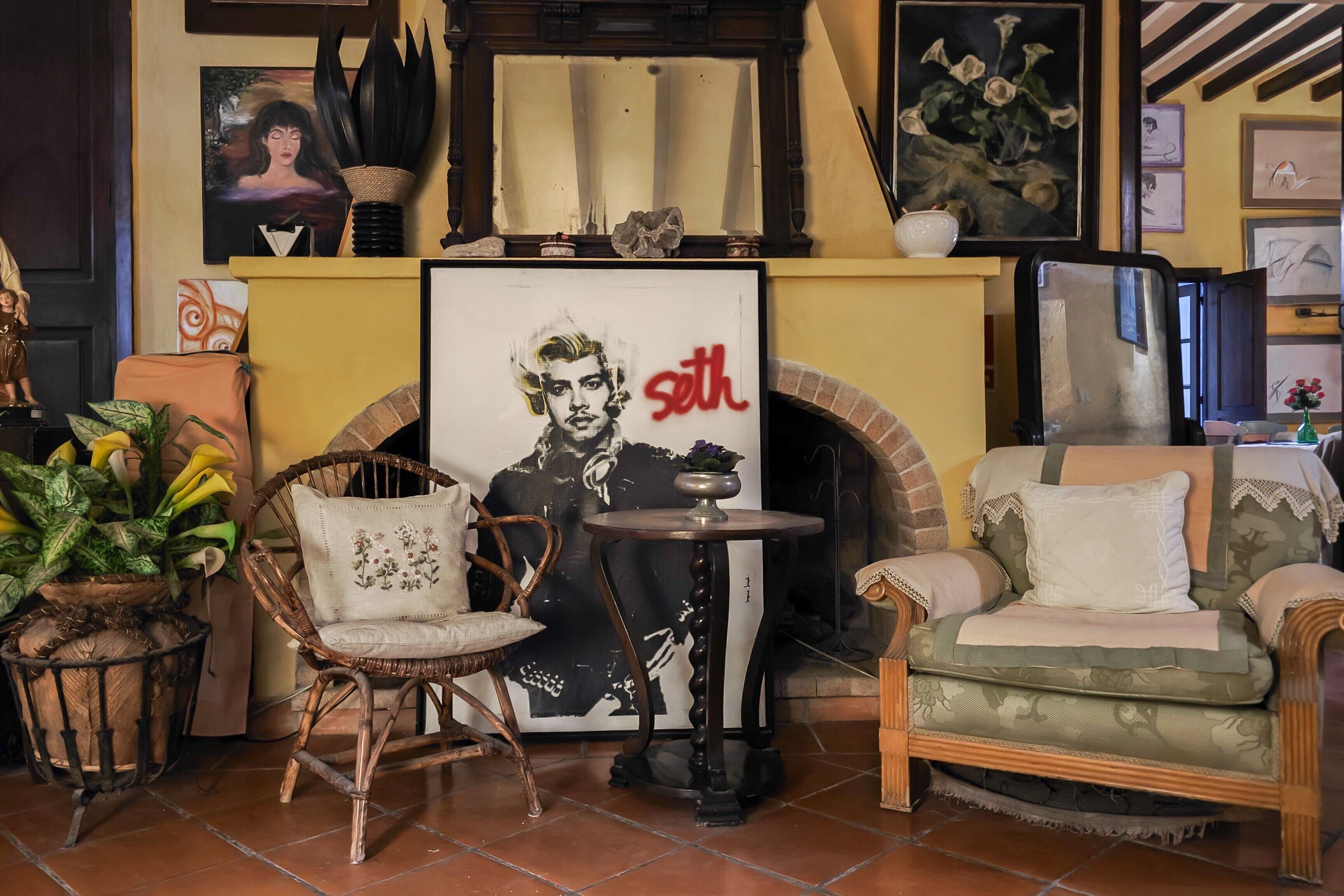 Una sala de estar acogedora con chimenea, un cartel enmarcado, un sillón de mimbre y un sofá verde.