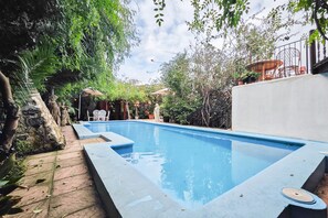 Een zwembad omringd door groen, met een terras en tuinmeubilair.