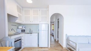 Cocina compacta con armarios blancos, microondas, refrigerador y un área de comedor con mesa y sillas.