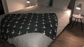 A bed with a black and white anchor pattern blanket, two bedside lamps, and striped pillows.