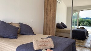 A bedroom with a bed, two sofas, a large mirror, and a view of greenery outside.