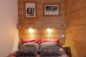 A wooden cabin room with a bed, pillows, a small table, and framed pictures on the wall.