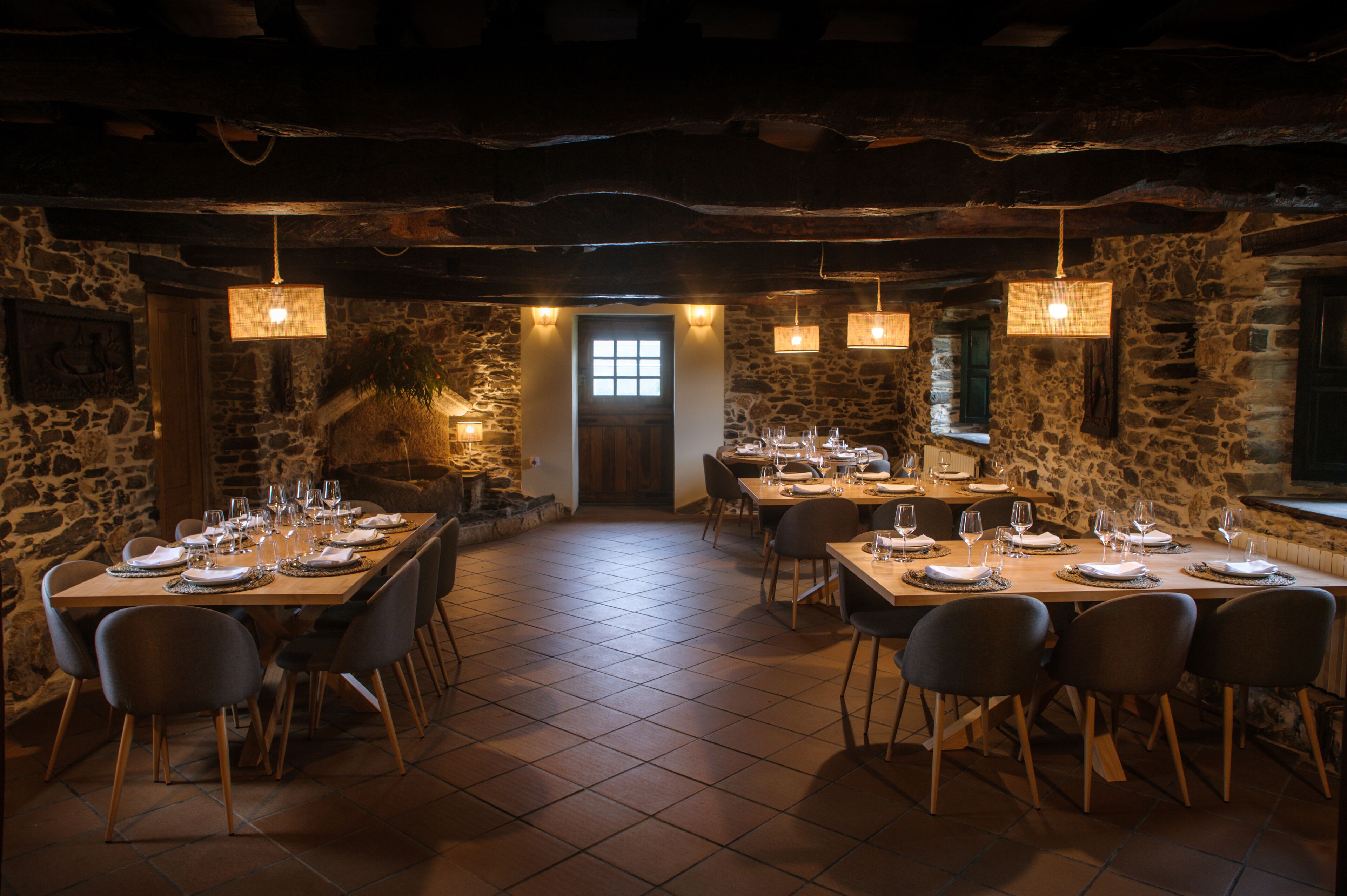 A restaurant with stone walls, wooden tables, and hanging light fixtures.