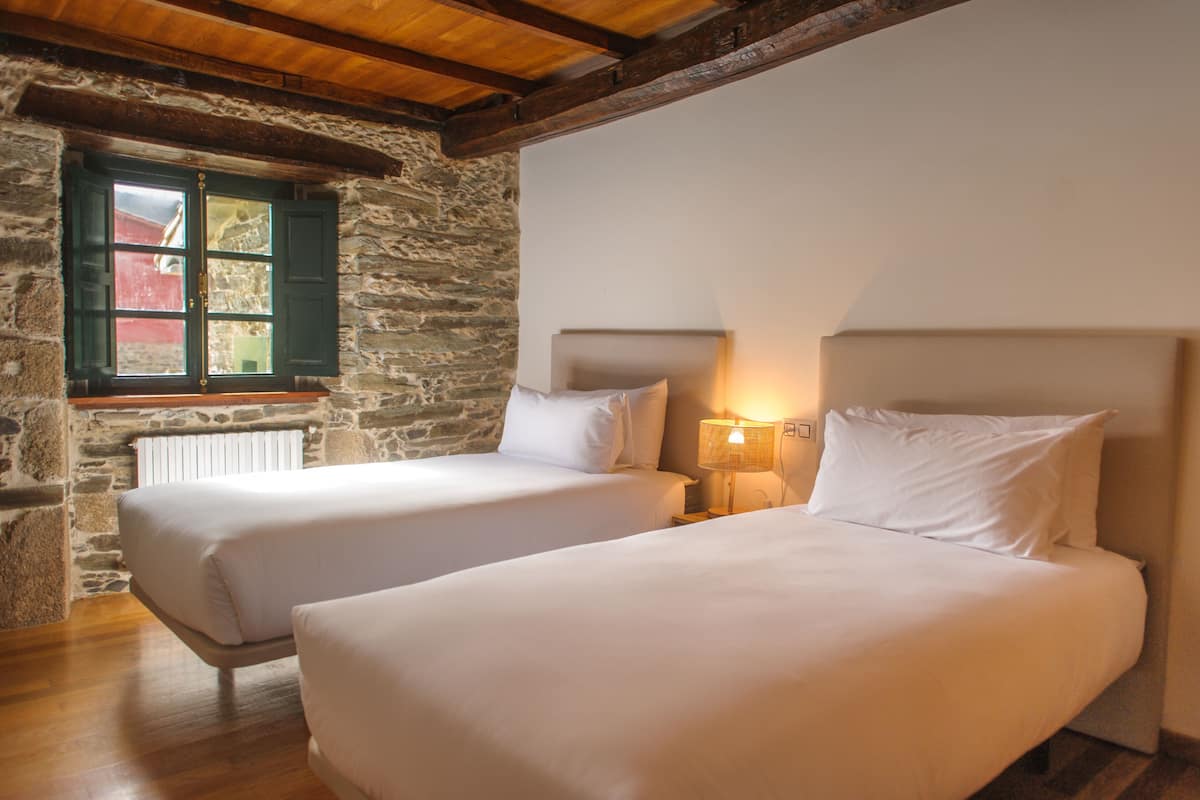 Deux lits jumeaux dans une chambre rustique aux murs de pierre et aux poutres apparentes.