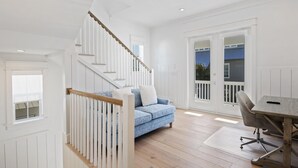 Ein geräumiger Raum mit einer Holztreppe, einem blauen Sofa, einem Esstisch mit einem Stuhl und großen Fenstern.