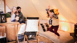A family inside a tent with a wooden chair, a small table with a lantern, and a sofa with cushions. - Luxury Glamping tent in Ouachita Mountains (Mena)