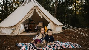 A tent with a simple interior layout, including a table and chairs, set in a forested area. - Luxury Glamping tent in Ouachita Mountains (Mena)