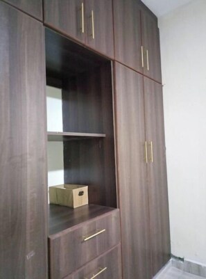A dark wooden wardrobe with three drawers and two doors, one with a mirror.