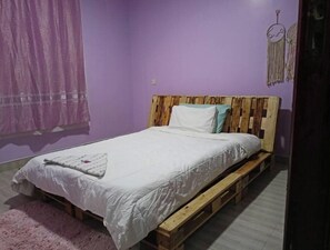 A room with a bed on a wooden pallet, a purple wall, and a dreamcatcher decoration.