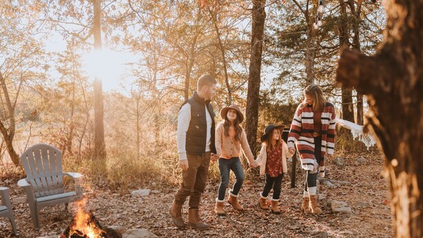 Una familia caminando por un bosque con una fogata y una hamaca.