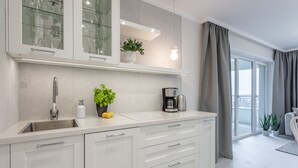 A modern kitchen with white cabinetry, a stainless steel sink, a coffee maker, and a potted plant.