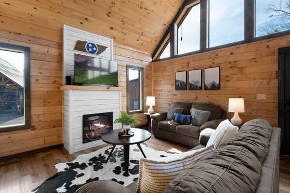 Un intérieur de chalet chaleureux avec une cheminée, des murs en bois, un téléviseur et un coin salon confortable.