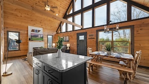 Une cuisine spacieuse dotée de plans de travail en granit, un coin repas avec des meubles en bois rustique, et de grandes fenêtres offrant une vue sur l’extérieur.