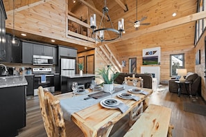 A spacious kitchen with modern appliances, a dining area with a wooden table set for six, and a cozy living room with a fireplace and comfortable seating.