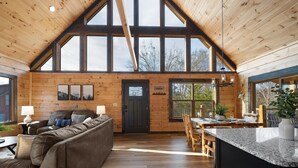 Un vaste espace de vie doté d’un haut plafond, de murs en bois, d’une porte sombre et d’un coin repas avec des meubles en bois et une grande fenêtre.