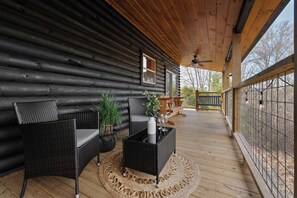 Une cabane en rondins dotée d’une terrasse en bois, de meubles en osier et de plantes en pot.