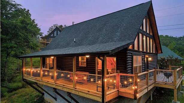 Une cabane en rondins dotée d’un balcon et d’un espace extérieur aménagé, entourée de verdure.