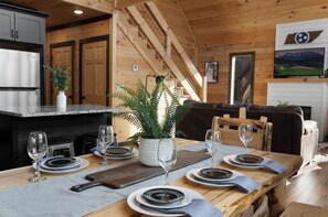 Un intérieur en bois comprenant une salle à manger avec une table dressée pour quatre personnes, un coin cuisine et un escalier.